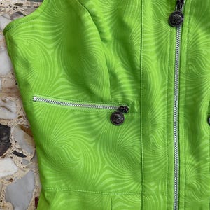 Może przedstawiać: Zielona sukienka bez rękaw&oacute;w z wirującym wzorem. Sukienka ma zamek błyskawiczny z przodu i srebrny zamek błyskawiczny na kieszeni.