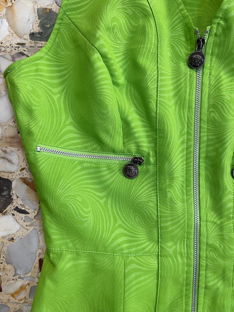 Może przedstawiać: Zielona sukienka bez rękaw&oacute;w z wirującym wzorem. Sukienka ma zamek błyskawiczny z przodu i srebrny zamek błyskawiczny na kieszeni.