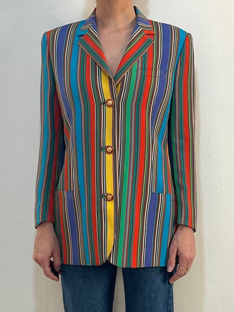 May include: A multi-colored striped blazer with a yellow stripe down the front. The blazer has four gold buttons.