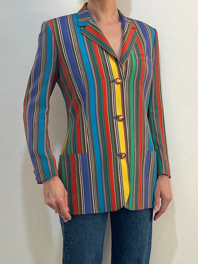 May include: A colorful striped blazer with a yellow stripe down the front and gold buttons. The blazer is made of a smooth fabric and has a classic cut.