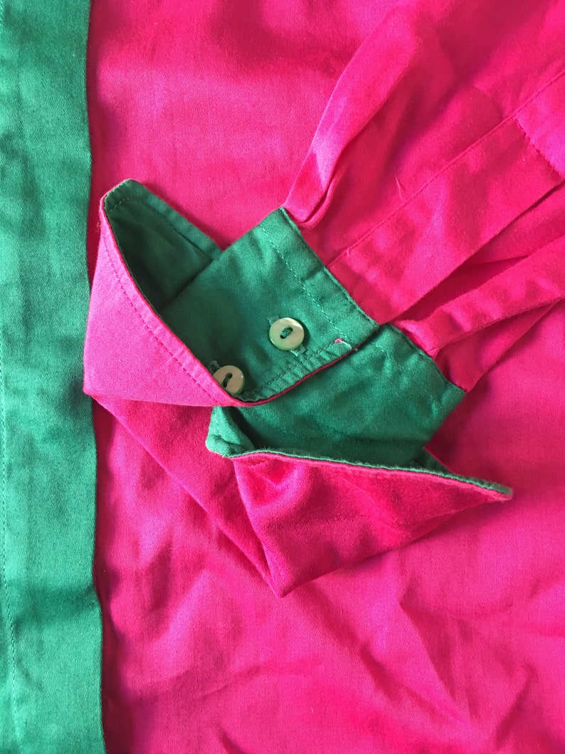 Puede incluir: Primer plano de una camisa rosa y verde con un pu&ntilde;o abotonado. La camisa est&aacute; hecha de una tela suave y sedosa.
