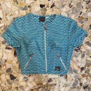 Op de afbeelding: Een kort, blauw-wit gestreept, met rits te sluiten topje met het woord "VERSACE" op de rits.