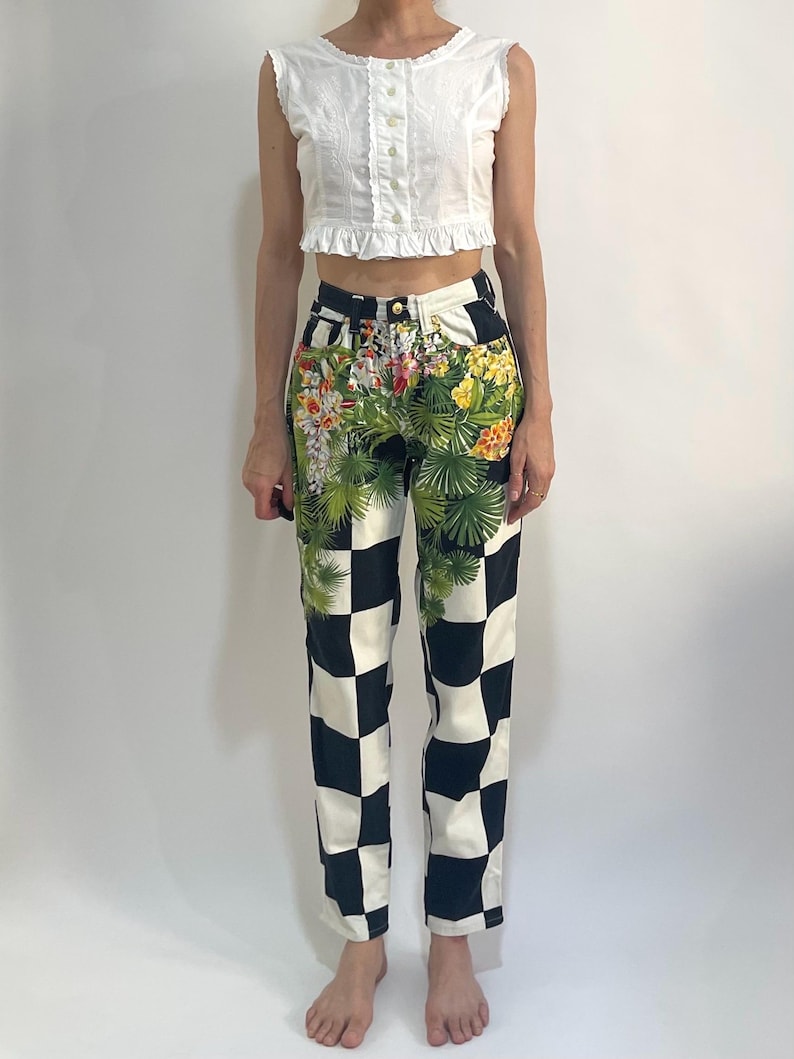 May include: A white sleeveless button-down top with a ruffled hem paired with high-waisted pants featuring a black and white checkered pattern on the lower half and a vibrant green tropical floral print on the upper hip and waist area.