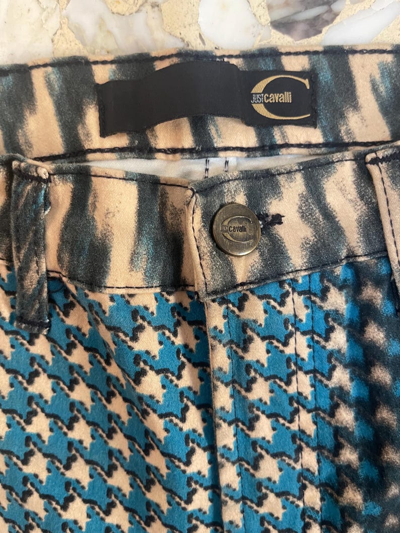 Puede incluir: Pantalones de patr&oacute;n azul y blanco con una cintura de estampado de cebra en blanco y negro. Los pantalones tienen un bot&oacute;n de metal dorado con el texto "Just Cavalli" en &eacute;l.