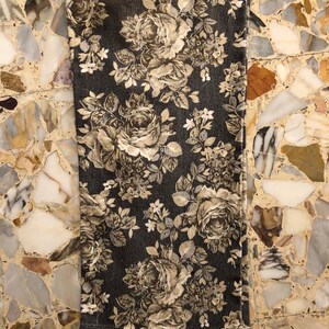 May include: A close-up of a dark grey fabric with a floral pattern. The flowers are a light beige colour and have a vintage look. The fabric has a subtle texture.