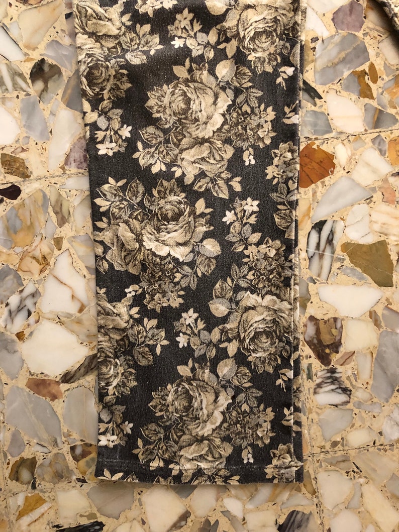 May include: A close-up of a dark grey fabric with a floral pattern. The flowers are a light beige colour and have a vintage look. The fabric has a subtle texture.