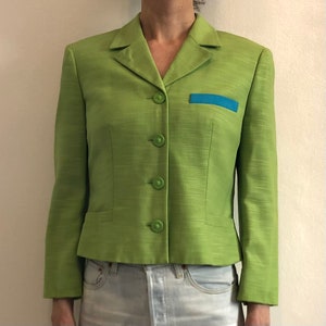 Pode incluir: Um blazer verde com uma guarni&ccedil;&atilde;o azul no bolso. O blazer tem um colarinho de entalhe e cinco bot&otilde;es na frente.