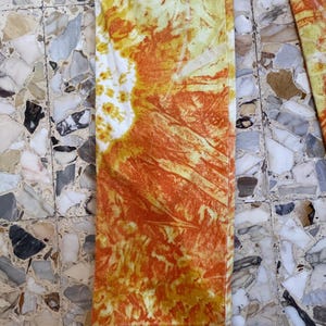 May include: A pair of orange and yellow tie-dye pants with a white background. The pants have a faded, vintage look.