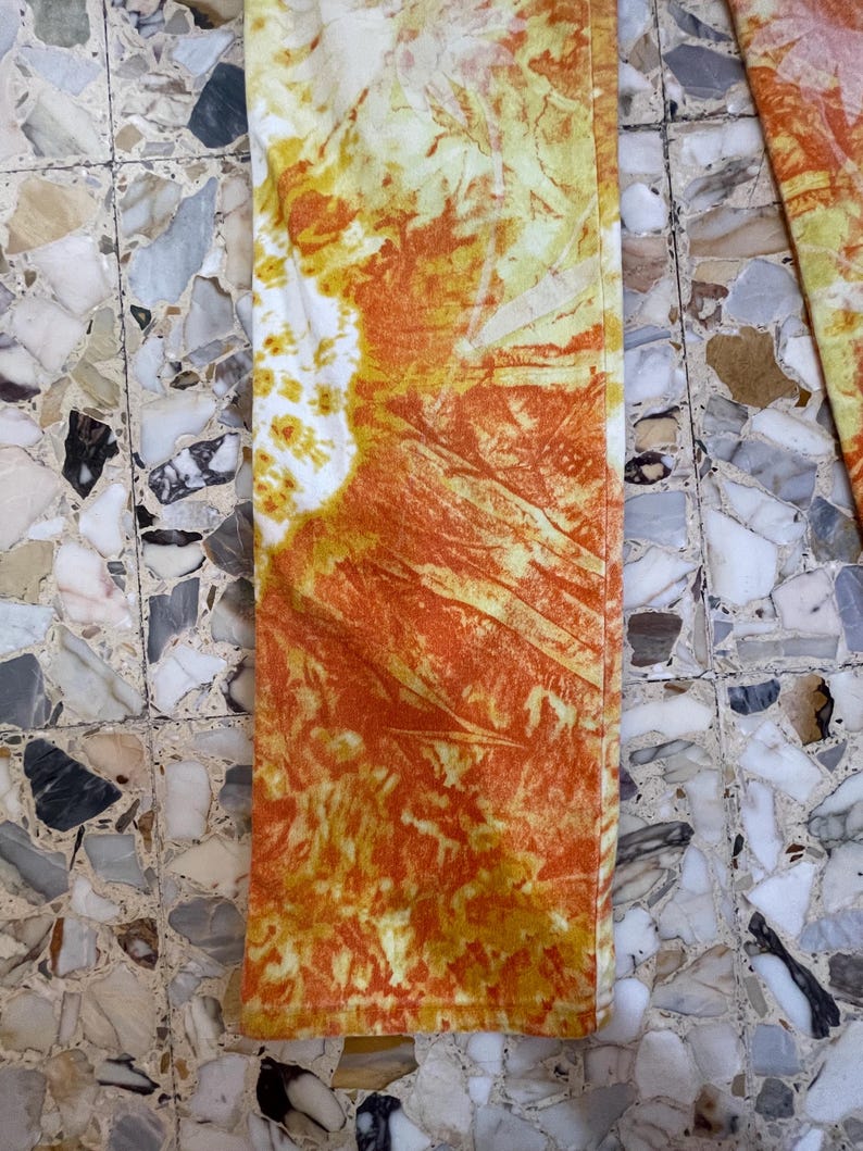 May include: A pair of orange and yellow tie-dye pants with a white background. The pants have a faded, vintage look.