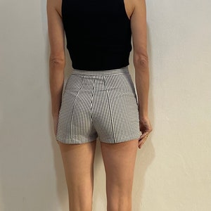 May include: A black sleeveless top paired with high-waisted shorts in a black and white checkered pattern. The shorts have a tailored fit. The outfit is simple and stylish, suitable for warm weather.