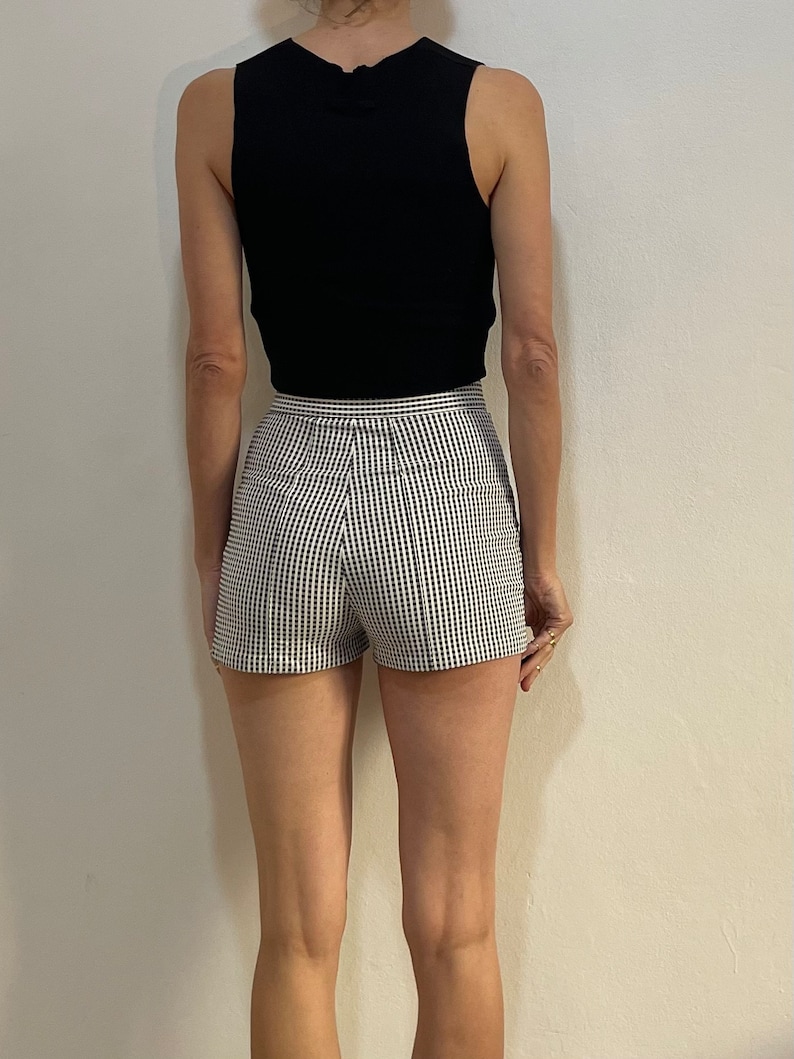 May include: A black sleeveless top paired with high-waisted shorts in a black and white checkered pattern. The shorts have a tailored fit. The outfit is simple and stylish, suitable for warm weather.