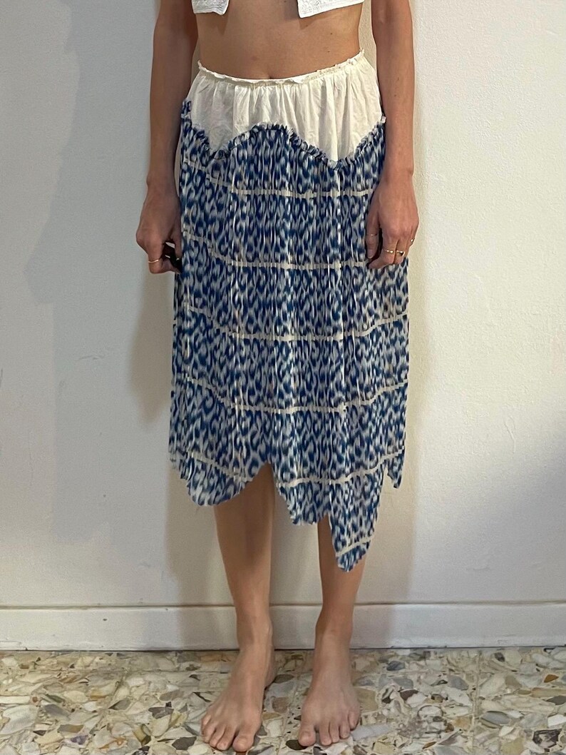 Op de afbeelding: Knie-lange rok met een witte tailleband en een blauw-wit patroon. De rok heeft een geschulpte rand en een vloeiend silhouet, ideaal voor een casual of bohemien look.
