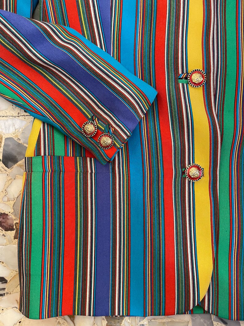 May include: A multi-colored striped blazer with gold buttons. The blazer has vertical stripes in shades of red, blue, green, yellow, and black.