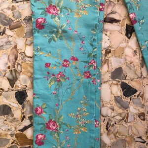 May include: A pair of blue pants with a floral print featuring pink, red, and yellow flowers. The pants have a straight leg and a relaxed fit.