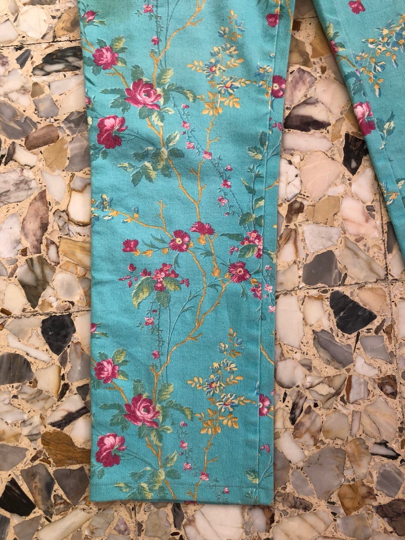May include: A pair of blue pants with a floral print featuring pink, red, and yellow flowers. The pants have a straight leg and a relaxed fit.