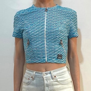 Op de afbeelding: Een blauw en wit gestreept getailleerd jack met een ritssluiting en een klein logo-patch met de tekst "VERSACE JEANS COUTURE".