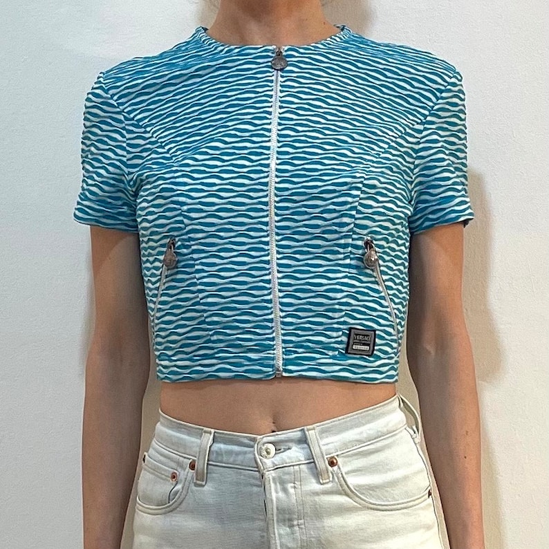 Op de afbeelding: Een blauw en wit gestreept getailleerd jack met een ritssluiting en een klein logo-patch met de tekst "VERSACE JEANS COUTURE".