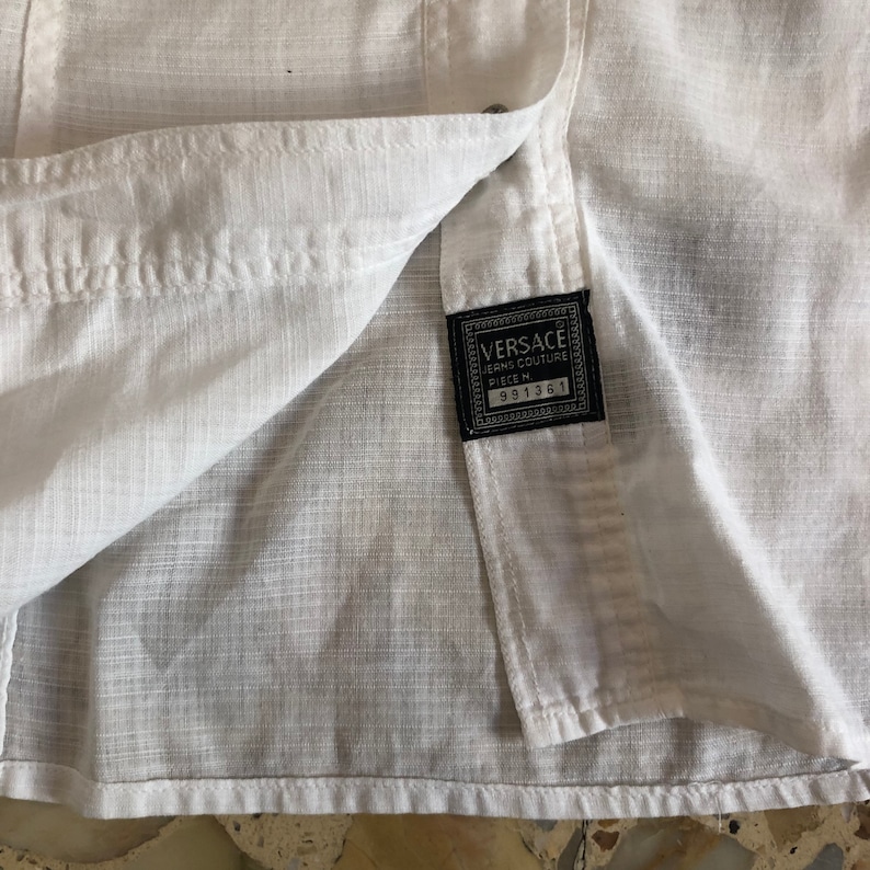 May include: White cotton shirt with a black label that reads "VERSACE JEANS COUTURE PIECE N. 991361".