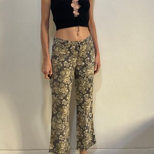 May include: A black sleeveless crop top with a lace-up detail at the front, paired with brown floral print trousers.