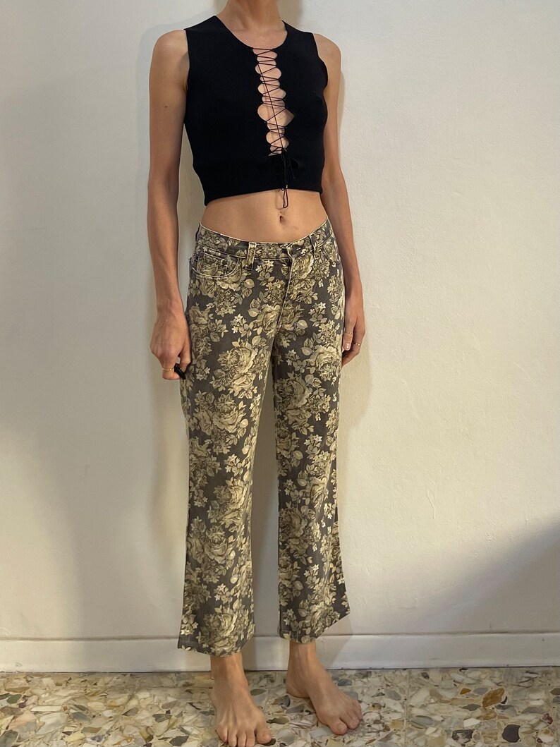 May include: A black sleeveless crop top with a lace-up detail at the front, paired with brown floral print trousers.