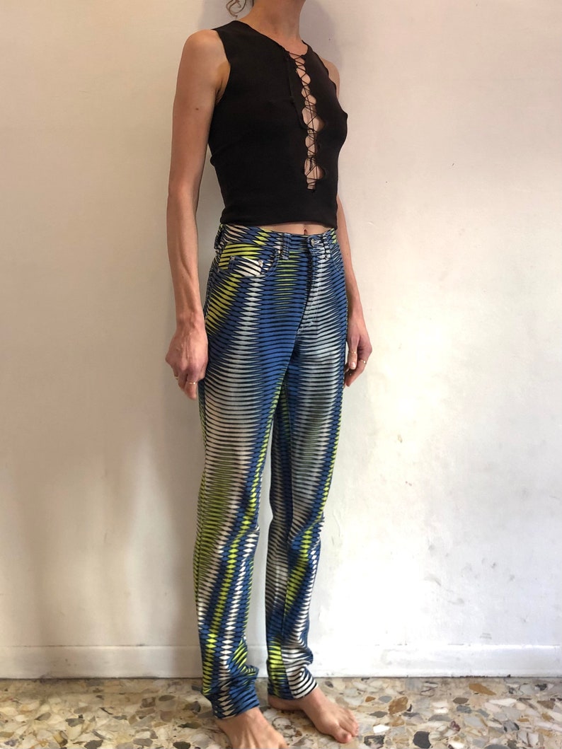 Puede incluir: Una camiseta negra sin mangas con un detalle de encaje en la parte delantera, combinada con pantalones de rayas azules y blancas con un patr&oacute;n geom&eacute;trico amarillo.