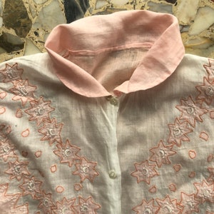Pu&ograve; includere: Una camicia di cotone bianco con colletto rosa e ricamo floreale delicato. Il ricamo &egrave; di colore rosa chiaro e presenta un motivo ripetitivo di piccoli fiori.