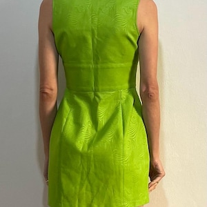 Może przedstawiać: Zielona sukienka bez rękaw&oacute;w z wirującym wzorem. Sukienka ma dekolt w kształcie litery V i dopasowany kr&oacute;j.