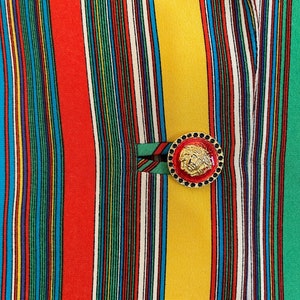 May include: A close-up of a striped fabric with a gold button featuring a lion's head design. The fabric is a mix of red, yellow, green, blue, and white stripes.