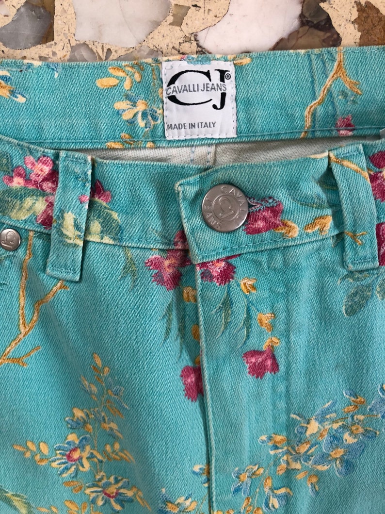May include: A pair of blue denim jeans with a floral print. The jeans have a label that reads "Cavalli Jeans" and "Made in Italy".