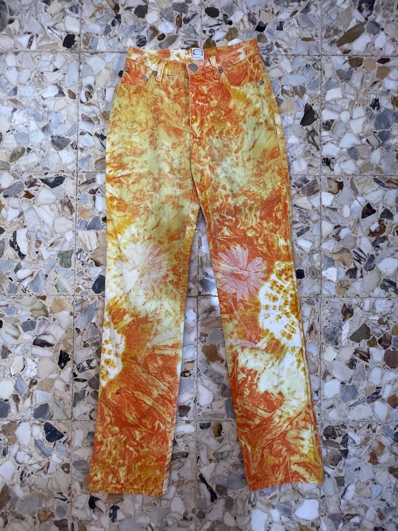 May include: Orange and yellow tie-dye jeans with a faded white pattern. The jeans have a high waist and a straight leg.