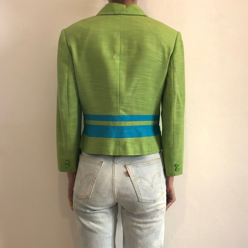 Pode incluir: Um blazer verde com uma faixa azul e verde na cintura.