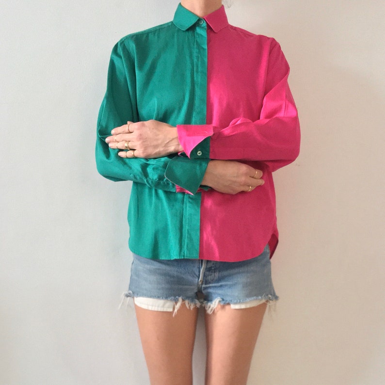 Puede incluir: Una camisa de manga larga con un dise&ntilde;o de bloques de color verde azulado y rosa. La camisa tiene un cuello abotonado y mangas largas con pu&ntilde;os abotonados. La camisa est&aacute; metida en unos pantalones cortos de mezclilla.