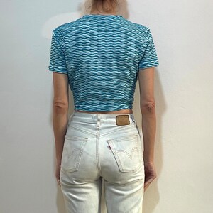 Op de afbeelding: Een blauw en wit gestreept crop top met korte mouwen en een ronde hals. Het topje is gemaakt van een rekbaar materiaal en heeft een golvend patroon.