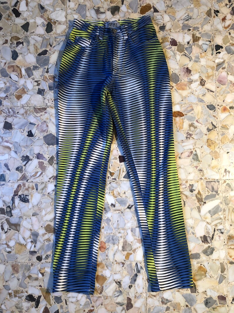 Puede incluir: Vaqueros con estampado azul, blanco y amarillo con la palabra "VERSACE" impresa en el bolsillo trasero.