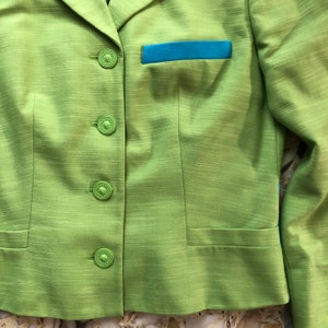 Pode incluir: Um blazer verde com uma aba de bolso azul e quatro bot&otilde;es. O blazer tem um tecido texturizado.