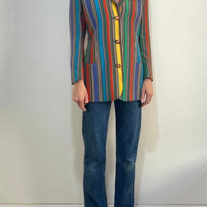 May include: A long-sleeved blazer with a colorful striped pattern in shades of blue, red, green, yellow, and brown. The blazer has a notched collar, a single-breasted closure, and four buttons.