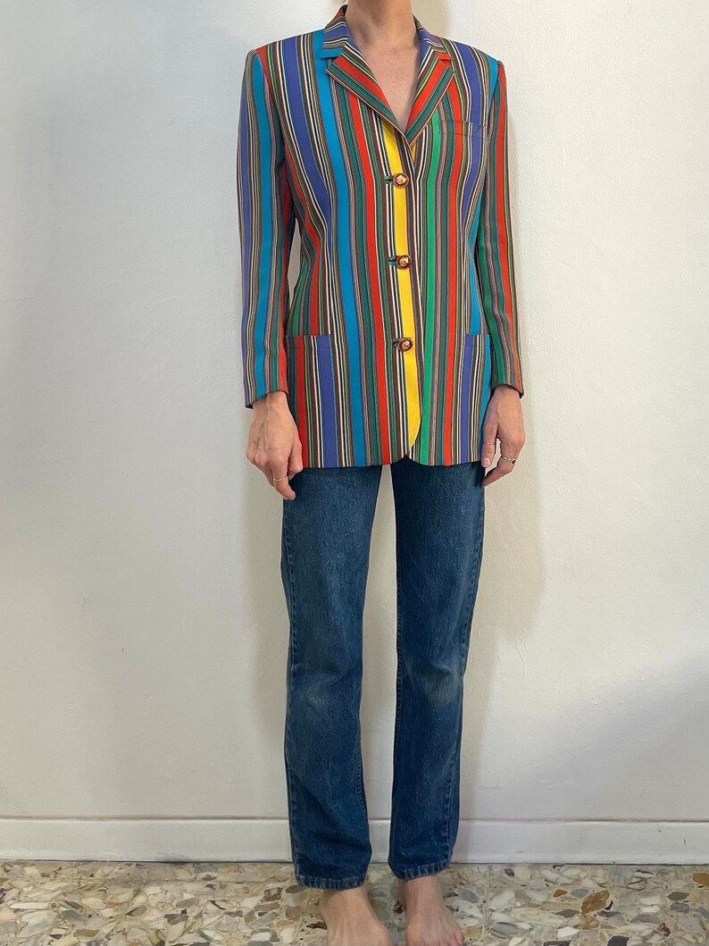 May include: A long-sleeved blazer with a colorful striped pattern in shades of blue, red, green, yellow, and brown. The blazer has a notched collar, a single-breasted closure, and four buttons.