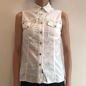 May include: White sleeveless button-down shirt with two flap pockets and silver buttons.