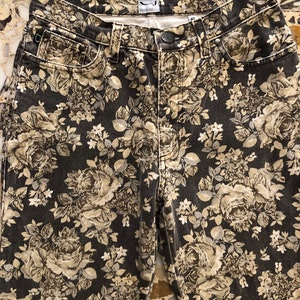 May include: Black denim jeans with a floral print in shades of beige and white. The jeans have a high waist and a straight leg.