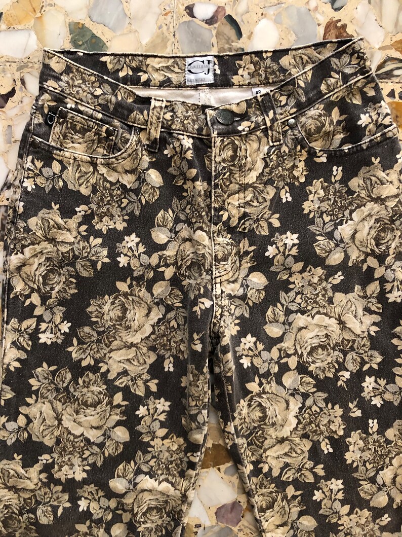May include: Black denim jeans with a floral print in shades of beige and white. The jeans have a high waist and a straight leg.