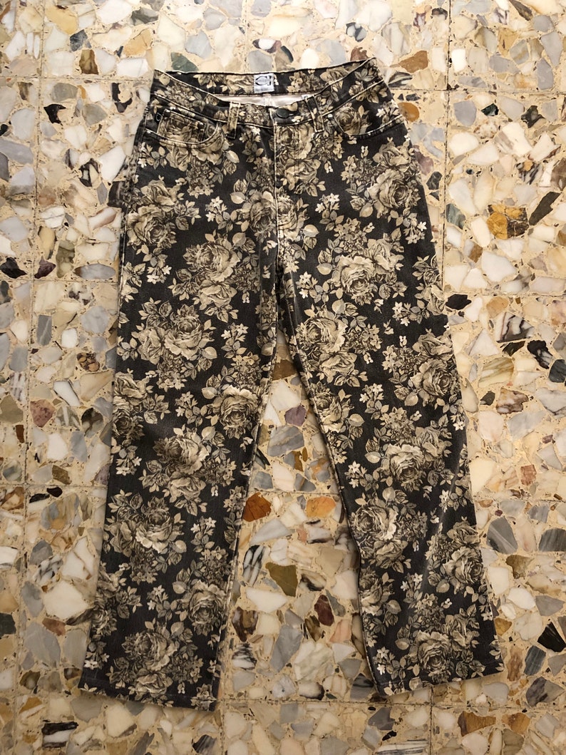 May include: Black denim trousers with a floral print in shades of beige and white. The print features roses and other flowers.