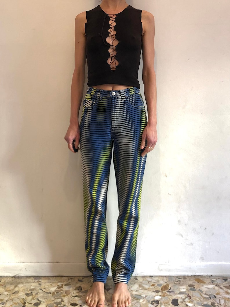 Puede incluir: Una persona lleva una camiseta negra sin mangas con un detalle de encaje y unos vaqueros con estampado azul y verde.