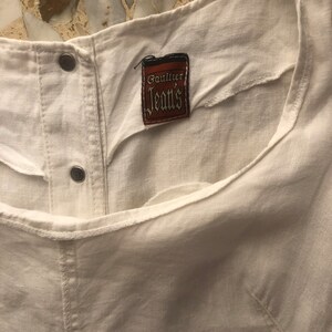 May include: White linen top with a brown label that says "Gaultier Jeans".
