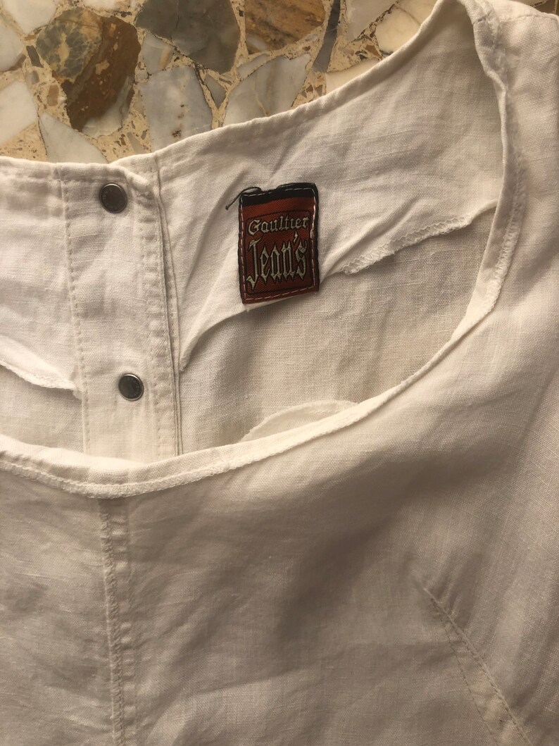 May include: White linen top with a brown label that says "Gaultier Jeans".