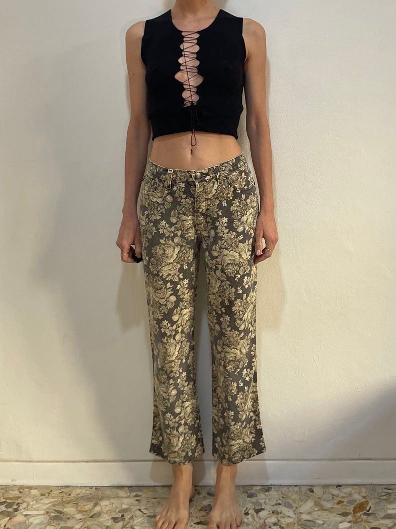 May include: A black sleeveless crop top with a lace-up detail at the front, paired with grey floral print trousers.