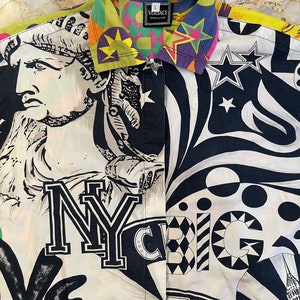K&ouml;nnte beinhalten: Ein wei&szlig;es Hemd mit Kn&ouml;pfen und einem schwarzen, wei&szlig;en und gelben Druck mit der Freiheitsstatue, den Worten "NY" und "Big City" sowie Sternen. Der Kragen ist ein mehrfarbiger Druck mit dem Wort "VERSACE" in einem schwarzen Rechteck.