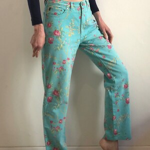 May include: A pair of light blue jeans with a floral print. The flowers are pink, red, and yellow. The jeans have a straight leg and a high waist.