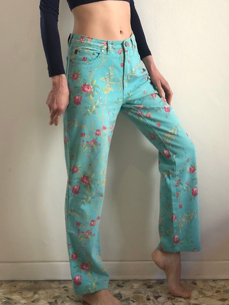 May include: A pair of light blue jeans with a floral print. The flowers are pink, red, and yellow. The jeans have a straight leg and a high waist.