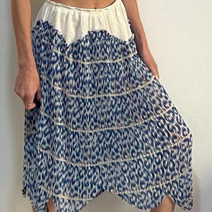 Op de afbeelding: Een gelaagde rok met een witte tailleband en een blauw-wit dierenprint ontwerp. De rok heeft een geschulpte zoom en is gemaakt van een lichte stof. De rok is knielang en heeft een vloeiend silhouet.