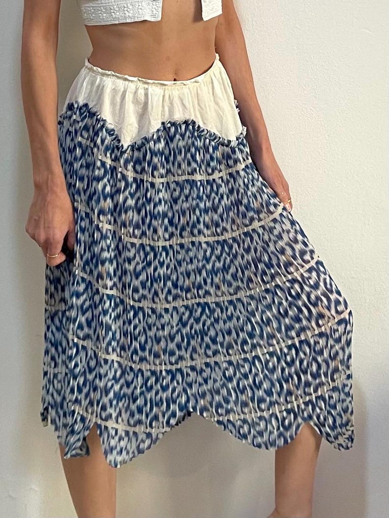 Op de afbeelding: Een gelaagde rok met een witte tailleband en een blauw-wit dierenprint ontwerp. De rok heeft een geschulpte zoom en is gemaakt van een lichte stof. De rok is knielang en heeft een vloeiend silhouet.